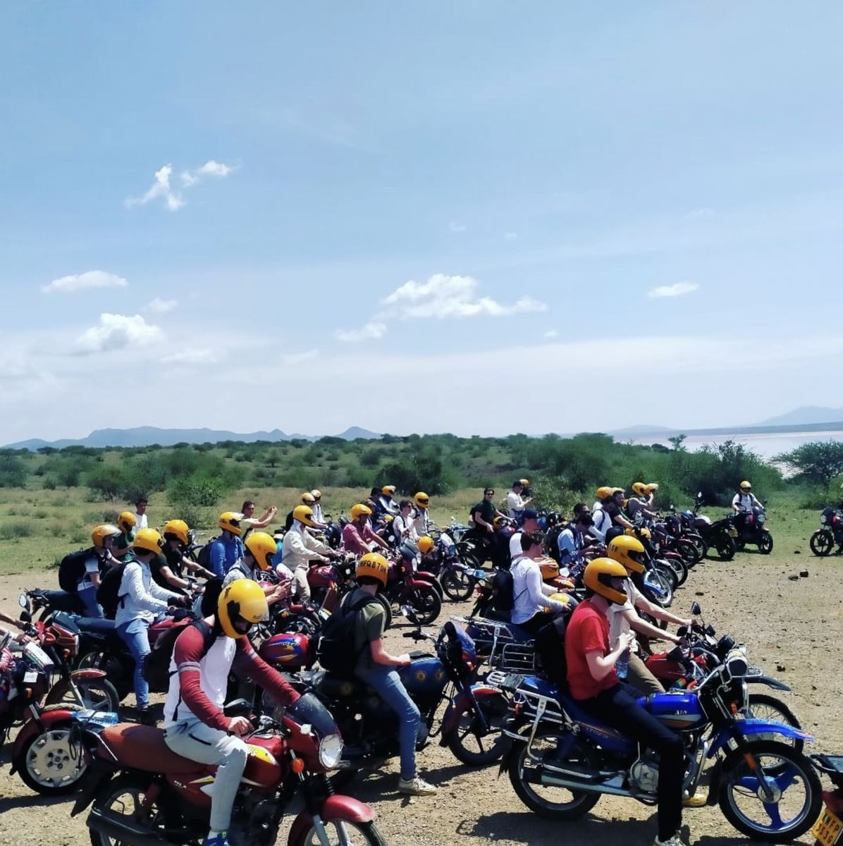 Riders in yellow helmets lined up near a lake